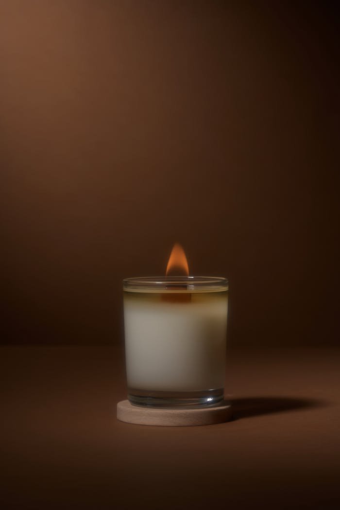 A minimalist photo of a single burning candle in a glass holder, emanating a tranquil glow, set against a warm, muted background.